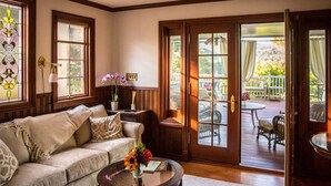 A cozy living room with a sofa, a coffee table with a vase of flowers, and a view of an outdoor deck through a glass door. - Mountain View Retreat (Fairfax)