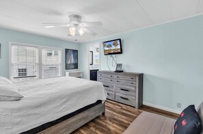 Une chambre à coucher comprenant un lit, une commode, un téléviseur et un ventilateur de plafond.