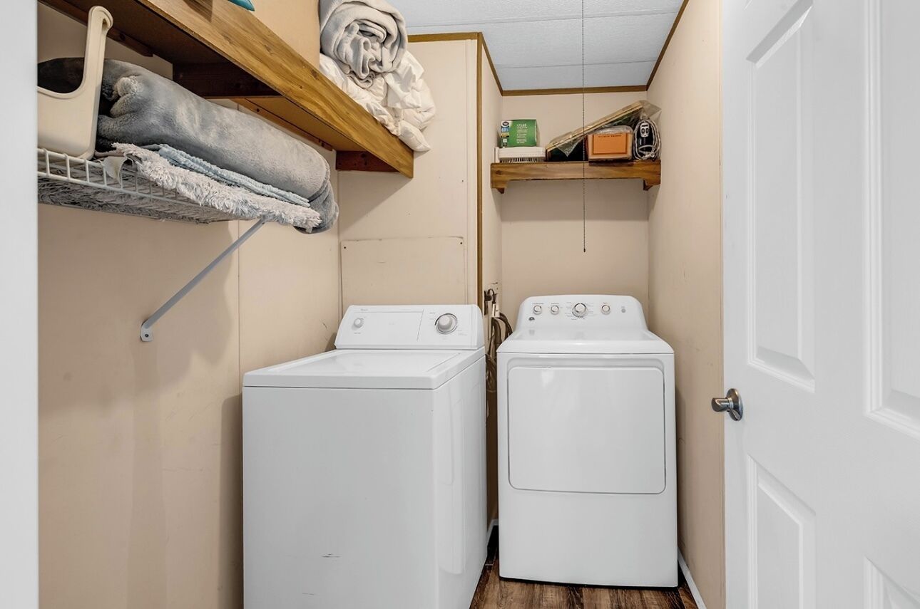 A laundry room with two white washing machines, wooden shelves above holding folded towels, and a door to the right.