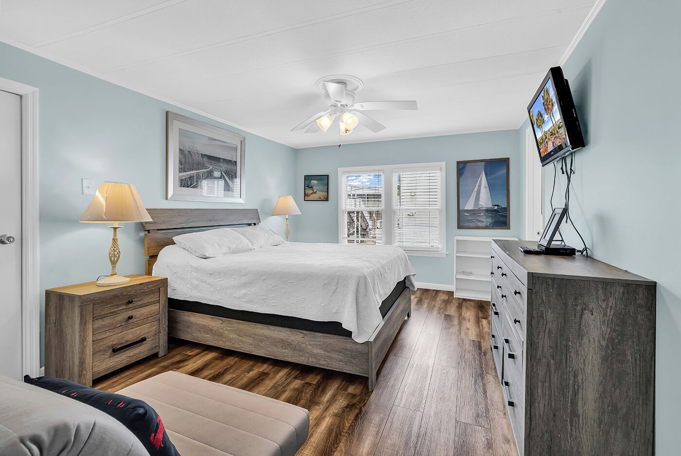 Een slaapkamer met een bed, nachtkastjes, een bureau, een televisie en een plafondventilator.