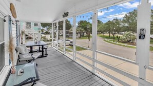 Área externa coberta com deck de madeira, corrimãos brancos e vista para uma rua residencial.