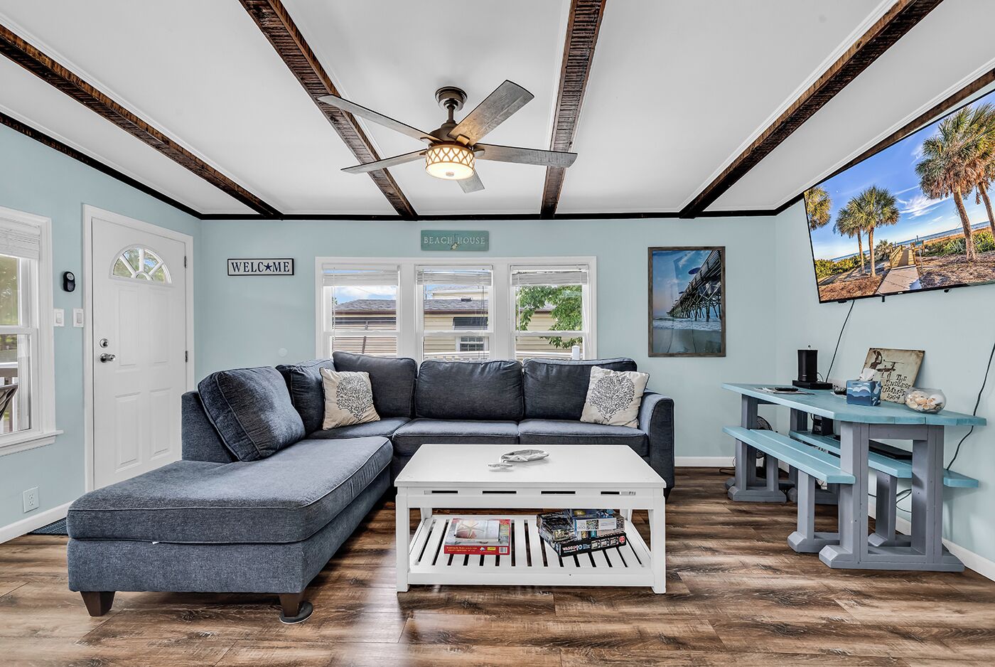 Un salon comprenant un canapé d’angle, une table basse, un ventilateur de plafond et un téléviseur fixé au mur.