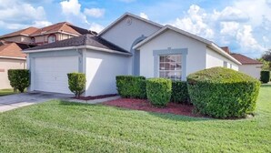 A single-story house with a white exterior, a garage, and a well-maintained lawn with trimmed bushes. - Canary Island by Orlando Short Term (Davenport)