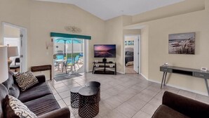 A living room with a sofa, coffee table, and TV. There is a ceiling fan, a door leading to a balcony, and a painting on the wall. - Canary Island by Orlando Short Term (Davenport)