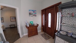 A hallway with a wooden door, a glass display case with plates, a bench, and a painting on the wall.