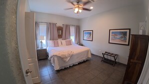 A bedroom with a bed, a ceiling fan, a nightstand, a window with curtains, and two framed pictures on the wall.