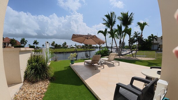 A patio with a view of a body of water, outdoor furniture, and palm trees.
