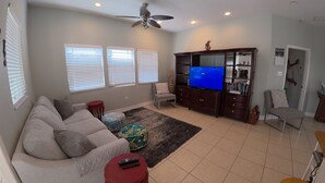 A living room with a sofa, ottoman, TV, and ceiling fan.