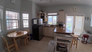 A kitchen with a refrigerator, stove, sink, and dining area with chairs and a table. - Tua'r  Mor (seaward) a beautiful guest home  overlooking the north sound. (Bodden Town)