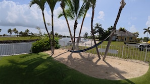 A hammock between palm trees, a fenced area, and a body of water.