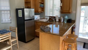 A kitchen with a stainless steel refrigerator, wooden cabinets, a granite countertop, a sink, a microwave, and a coffee maker.