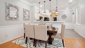 A dining area with a wooden table and four upholstered chairs, a chandelier, and decorative mirrors on the walls. - Rent My NOLA Jewel, Luxury Accommodations (New Orleans)