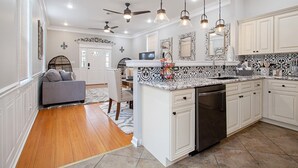 A spacious kitchen with white cabinetry, a marble countertop, and a dishwasher. There are ceiling fans and pendant lights. - Rent My NOLA Jewel, Luxury Accommodations (New Orleans)