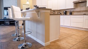 A modern kitchen with white cabinets, a granite countertop, and stainless steel bar stools. - Sunrise Valley Villa by Orlando Short Term (Kissimmee)