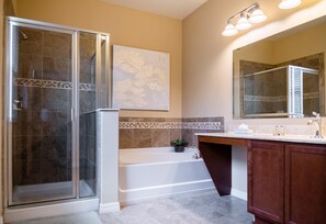 A bathroom with a glass-enclosed shower, a bathtub, a vanity with a mirror, and a wall-mounted light fixture. - Sunrise Valley Villa by Orlando Short Term (Kissimmee)