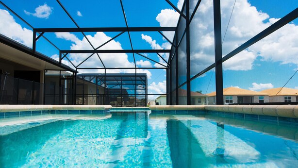 A swimming pool with clear blue water, surrounded by a modern architectural structure with glass and metal elements. - Sunrise Valley Villa by Orlando Short Term (Kissimmee)