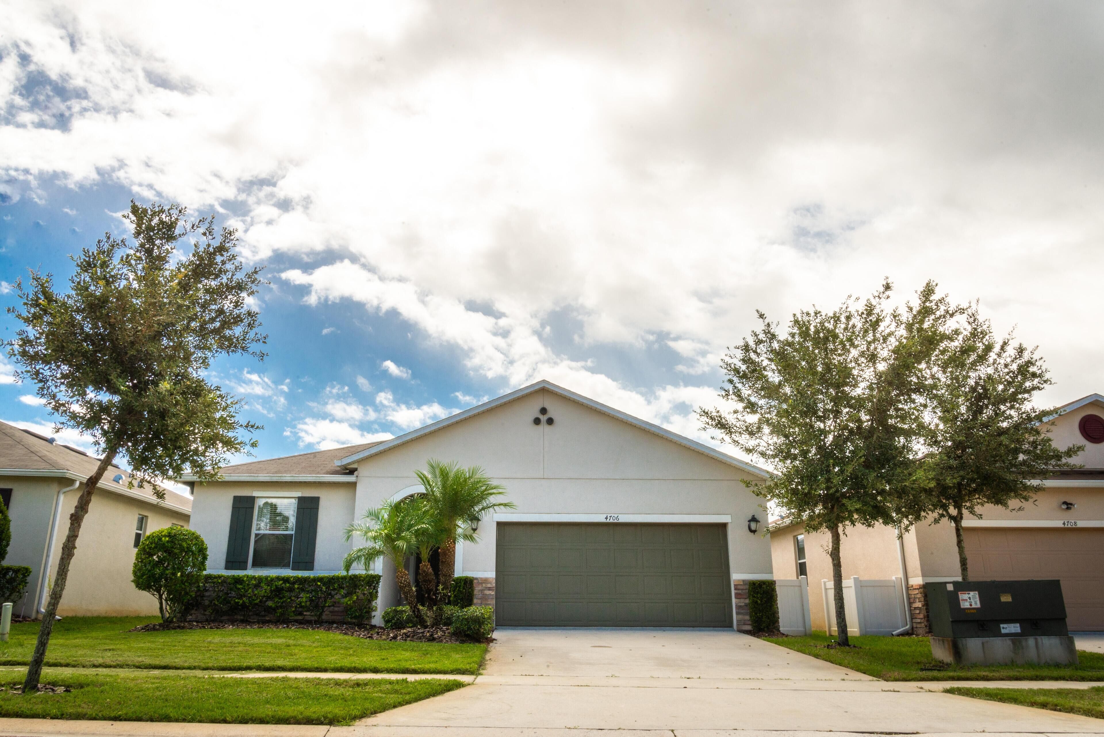 A single-story residential building with a garage, surrounded by well-maintained lawns and trees.