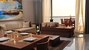 A modern living room with a sofa, a dining table set for two, and a view of the ocean through large windows. - 5 star Diamond Private Residence Club (Marina Vallarta)