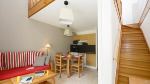 Un salon avec un canapé, une table à manger avec des chaises, un coin cuisine équipé d’un four à micro-ondes et un escalier en bois.