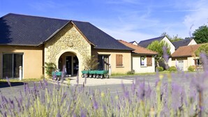 A building with a stone facade, a green cart, and a clear blue sky. - Maisonnette Abordable 5mn de Lascaux (Montignac)