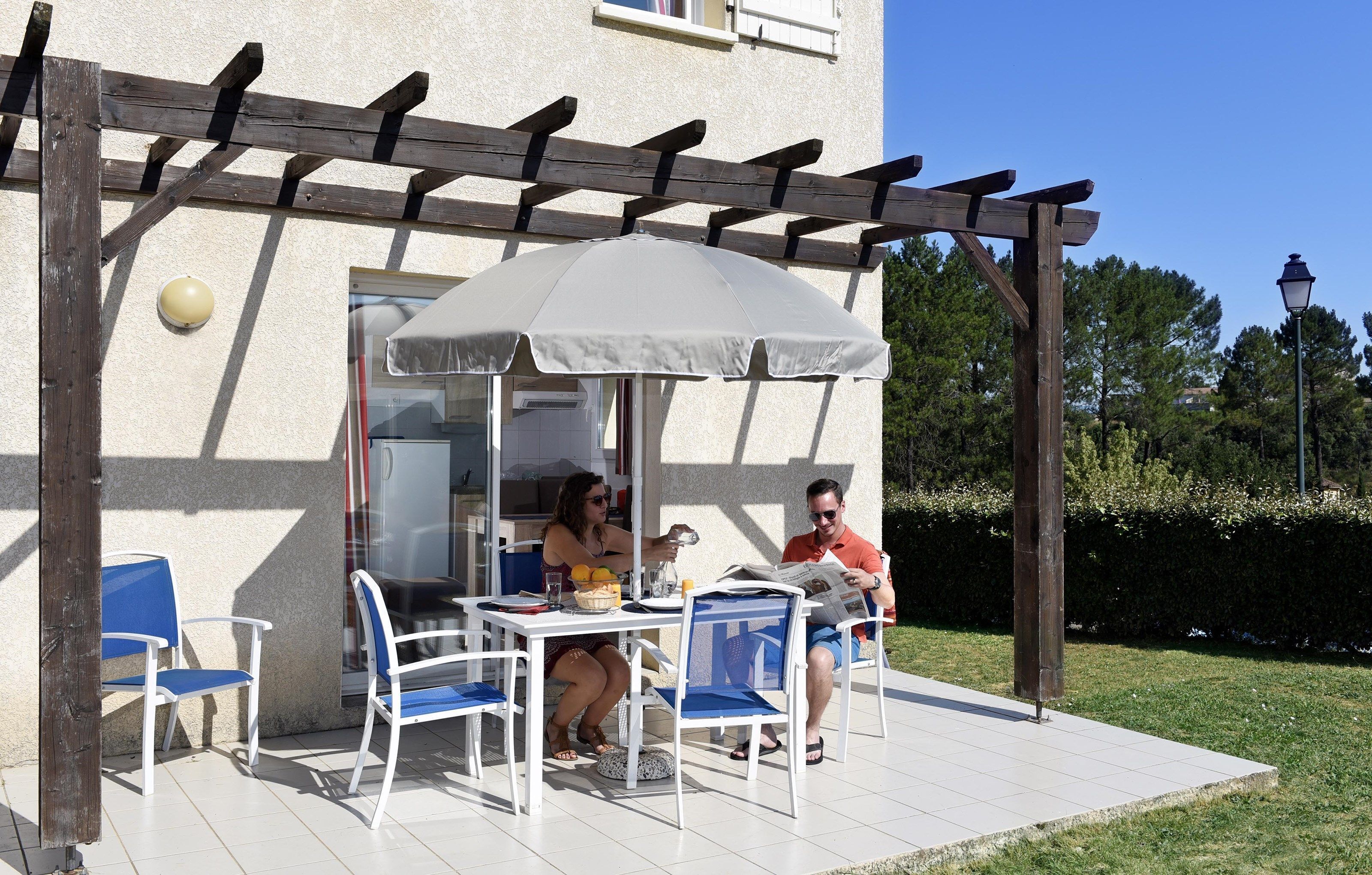 Un patio al aire libre con pérgola, sillas blancas y una mesa.