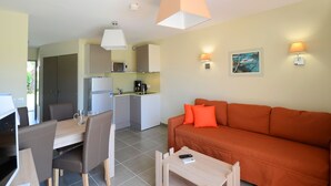 Un espacio habitable compacto con comedor, kitchenette y un sofá con cojines naranjas.