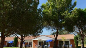 Un edificio con techo de tejas, mesas al aire libre con sombrillas azules y árboles circundantes.