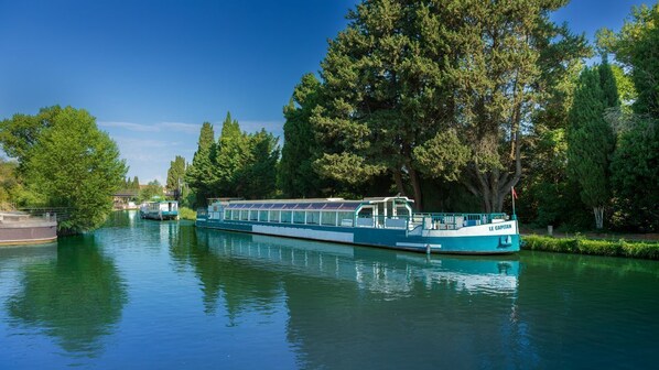 A riverboat with a covered deck, surrounded by trees and calm water.
