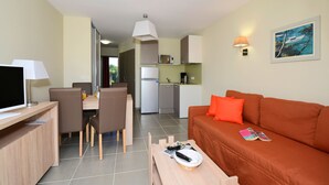 Un espacio habitable compacto con comedor, kitchenette y un sofá con una revista.