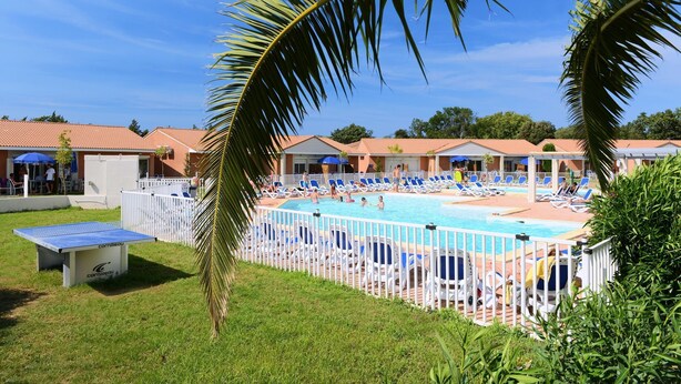Zona de piscina con sillones reclinables y una mesa, rodeada por una cerca blanca.