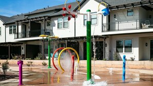 Un área de juegos con agua, con estructuras coloridas y un edificio al fondo.