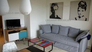 A living room with a grey sofa, a colorful coffee table, and a TV on a wooden cabinet.