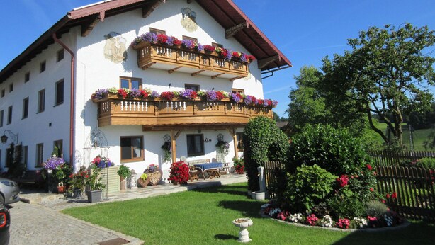 Ein zweistöckiges Gebäude mit einem Blumen geschmückten Balkon, einem gepflegten Rasen und einem Holzzaun.