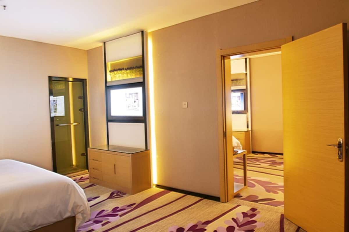 Quarto de hotel com cama, escrivaninha, espelho, guarda-roupa e porta para outro cômodo.