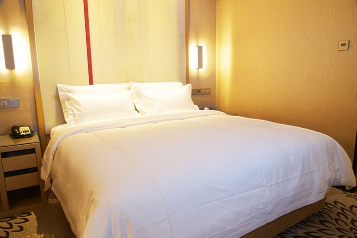 Quarto de hotel com uma cama grande, mesas de cabeceira e luminárias fixadas na parede.