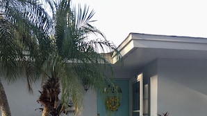 A house with a light blue door, a small porch, and a garden with palm trees and other plants. - Private Updated Mother In Law Apartment with Fenced Yard 4 miles from Siesta Key (Sarasota)