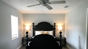 A bedroom with a black bed, two bedside tables with lamps, a ceiling fan, and a window on the left wall. - Private Updated Mother In Law Apartment with Fenced Yard 4 miles from Siesta Key (Sarasota)