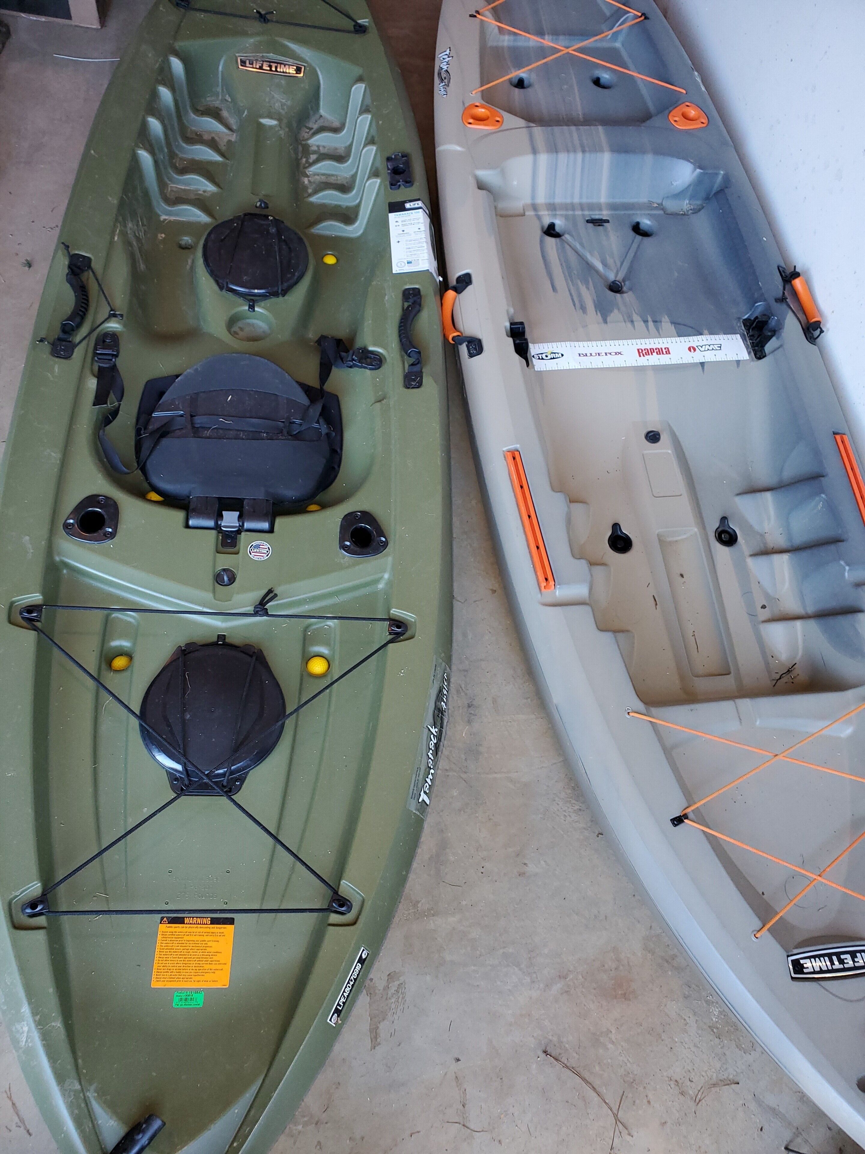 Two kayaks with seating and storage compartments, one green and one white, with safety labels and straps.