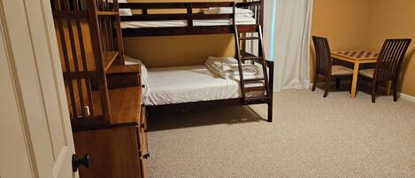 Una cama litera con escritorio y silla, piso alfombrado y una puerta con panel de madera.