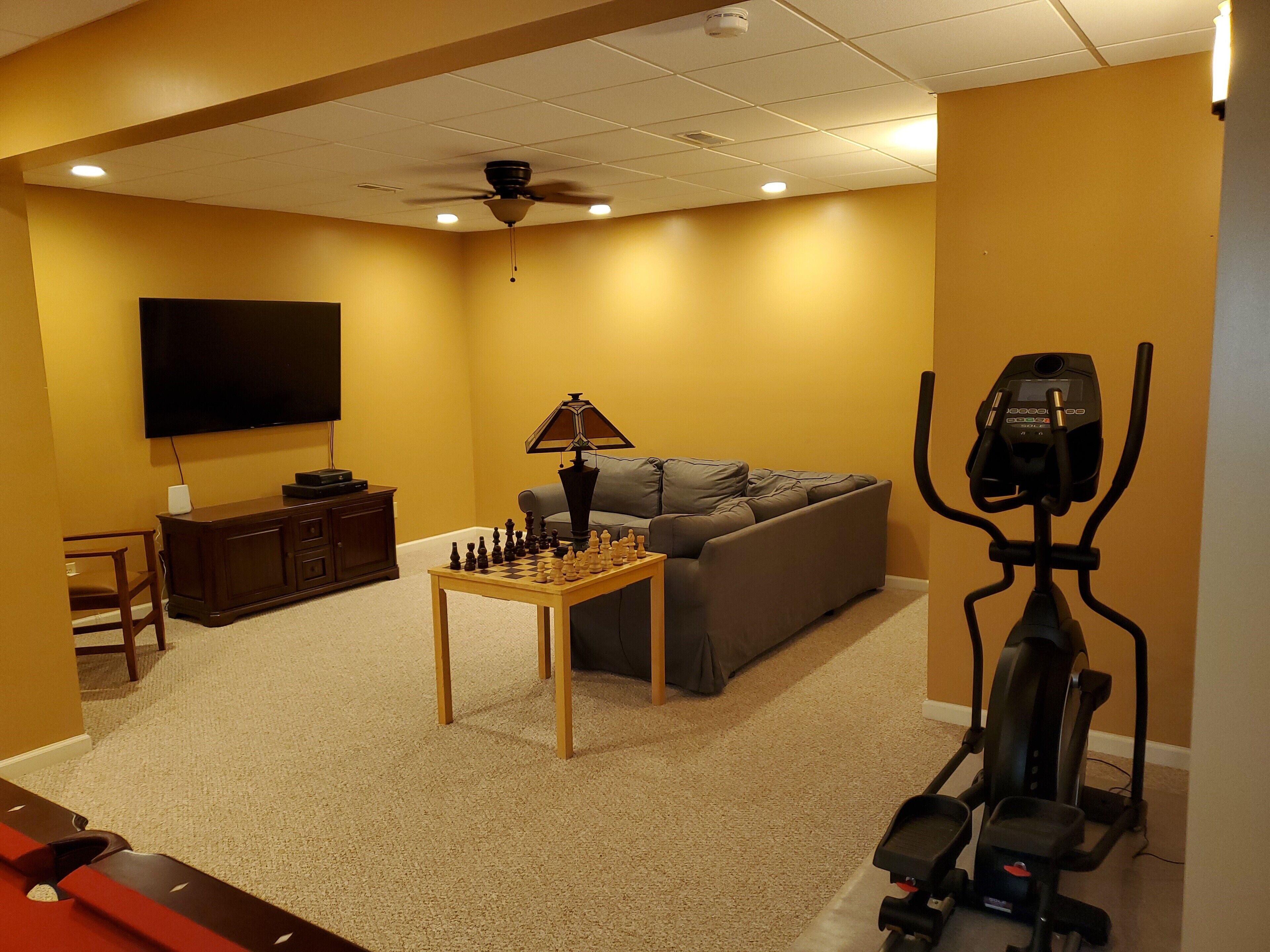 Uma sala de estar com sofá, mesa de xadrez, esteira e televisão.