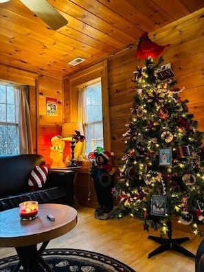 Een gezellig interieur van een blokhut met een versierde kerstboom, houten wanden, een open haard en een comfortabele zithoek.