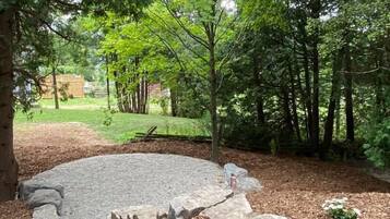 A circular stone patio surrounded by mulch and small plants, with trees in the background.
