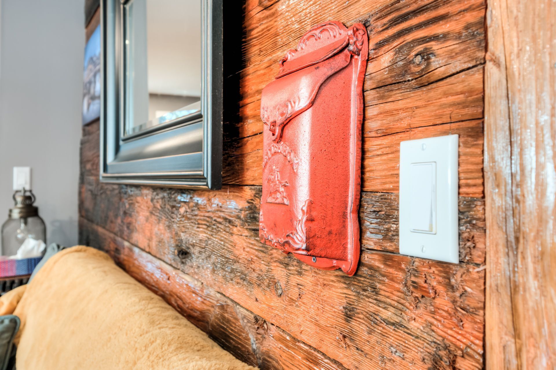A rustic wooden wall with a red leather bag hanging on it, a white light switch, and a mirror.