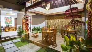 An outdoor dining area with wooden tables and chairs, surrounded by potted plants and a stone wall. - The Light Bali Villa (Seminyak)