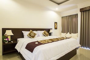 A neatly made bed with white linens and decorative pillows, a bedside table with a lamp and flowers, and a view of a window with curtains. - The Light Bali Villa (Seminyak)
