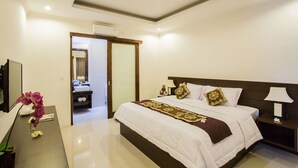 A modern hotel bedroom with a large bed, a bedside table with a lamp, a mirror, and a bathroom visible through an open door. - The Light Bali Villa (Seminyak)