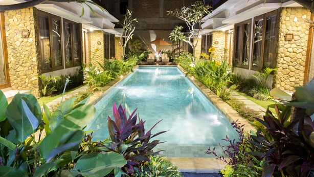A pool area with a stone wall, plants, and a canopy. - The Light Bali Villa (Seminyak)