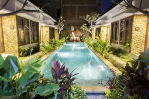 A pool area with a stone wall, plants, and a canopy. - The Light Bali Villa (Seminyak)