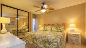A bedroom with a bed, two bedside lamps, a nightstand, a ceiling fan, and a large mirror.