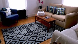 Een woonkamer met een blauwe fauteuil, een beige bank en een kamerbreed tapijt met dessin.